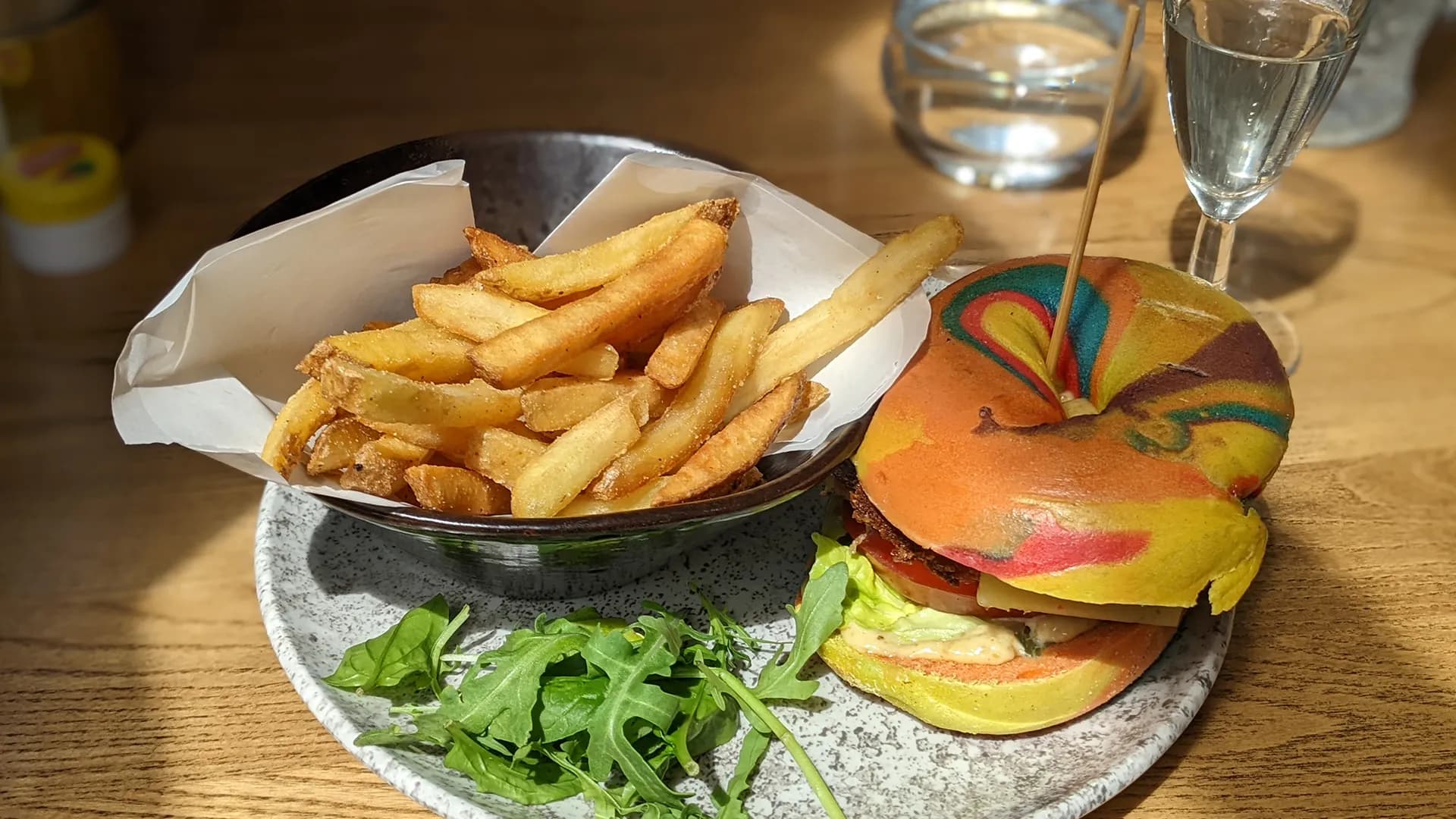 Colourful rainbow bagel burger and chips at Aluna